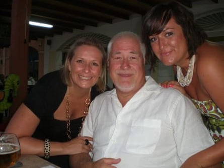 Natalie and Danielle stand either side Pete, who is sitting at a table