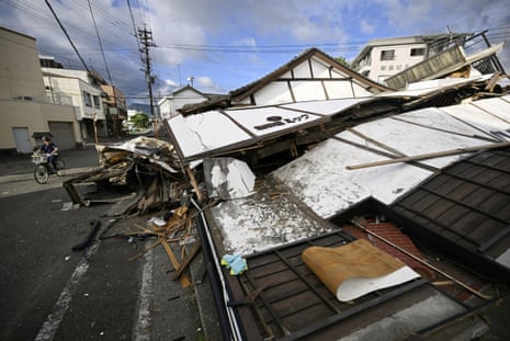 A person cycles past a collapsed building.