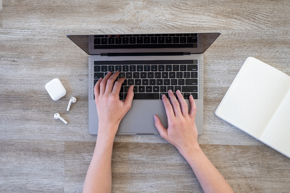 Hands typing on a silver laptop on a wooden desk, viewed from above